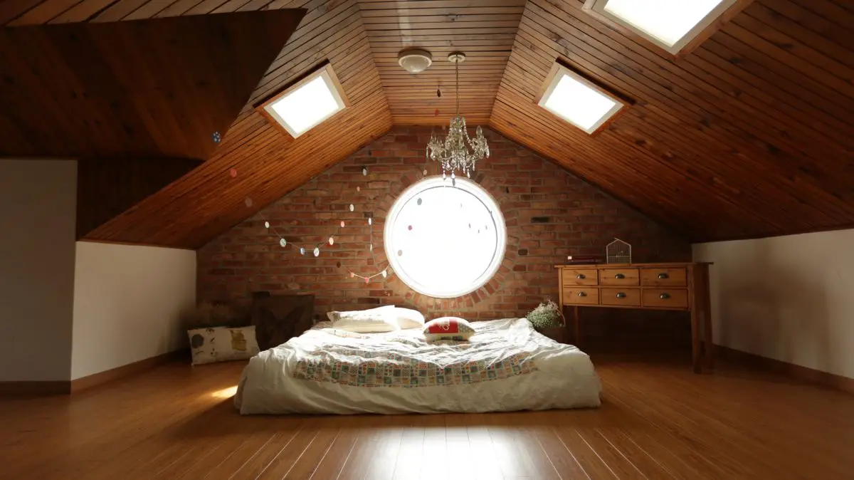 An attic bedroom with a sloped wood ceiling, a bed, and a small dresser under a round window
