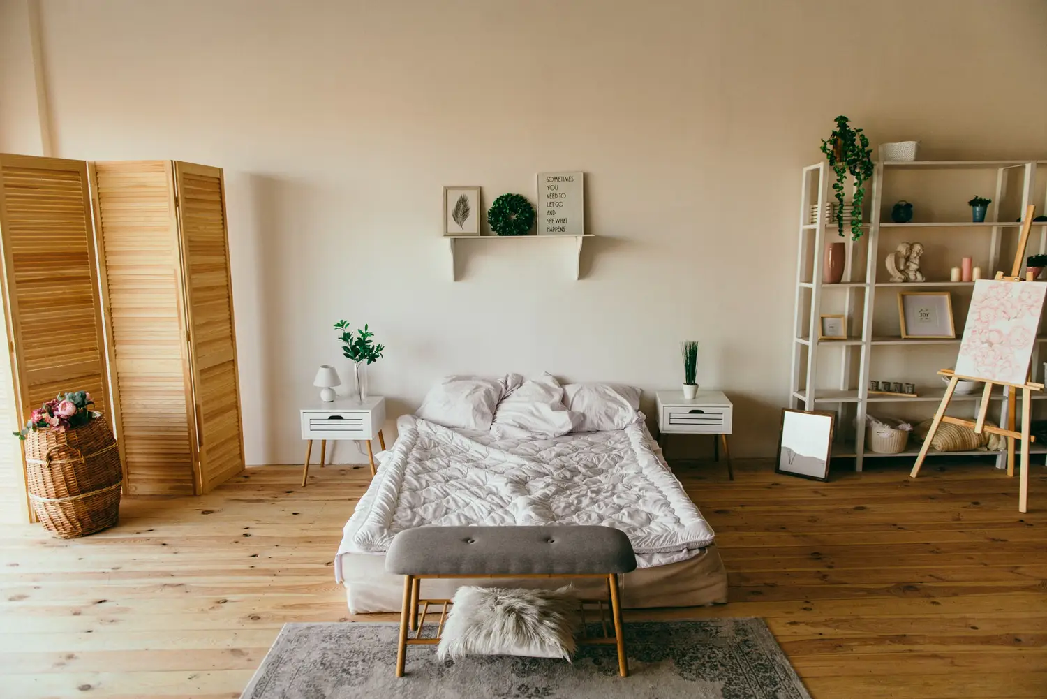 A platform bed between two white nightstands, with a tall open shelf to the right, on a light wood floor