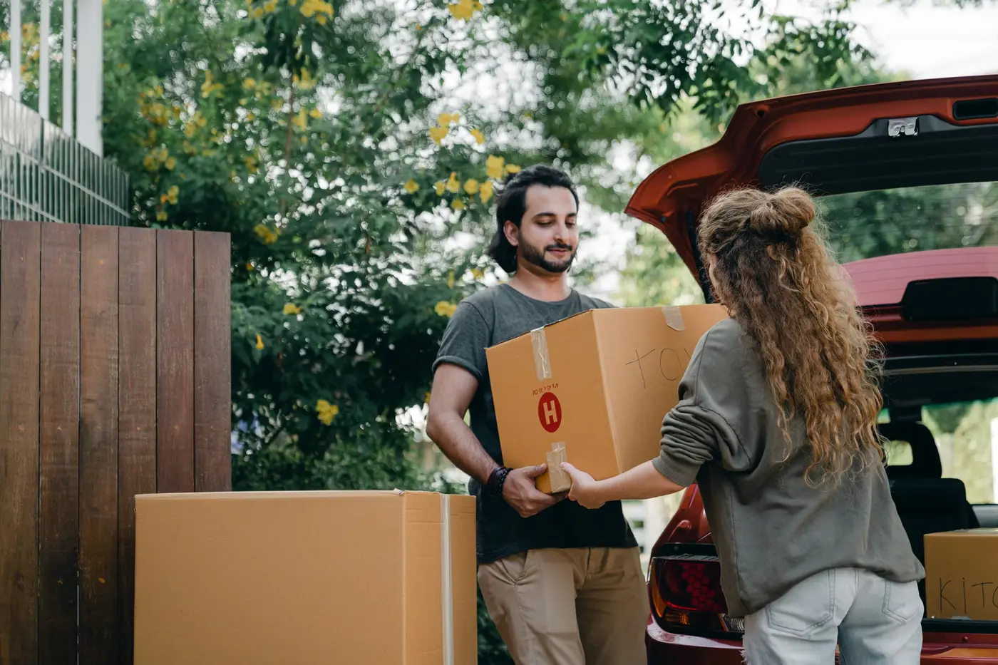 Two people handing a cardboard carton beside the open trunk of a car