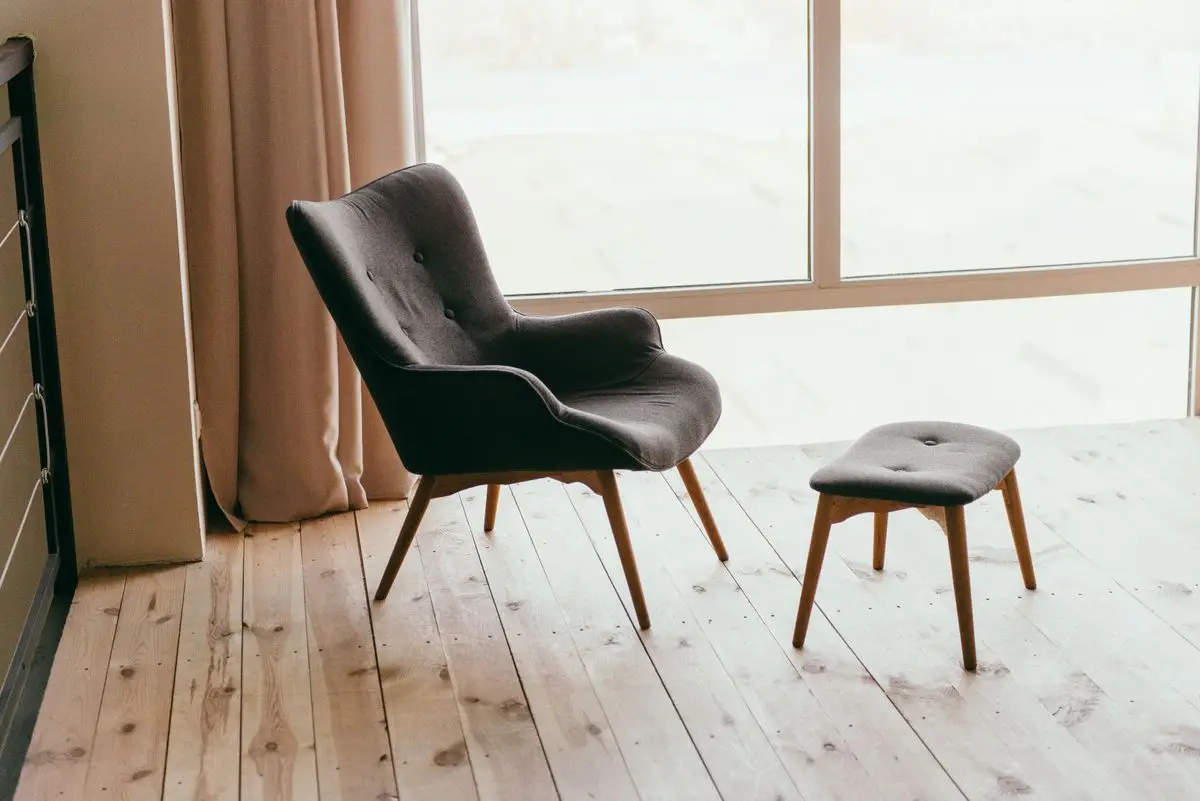 An armchair and ottoman on pale floorboards near a bright window