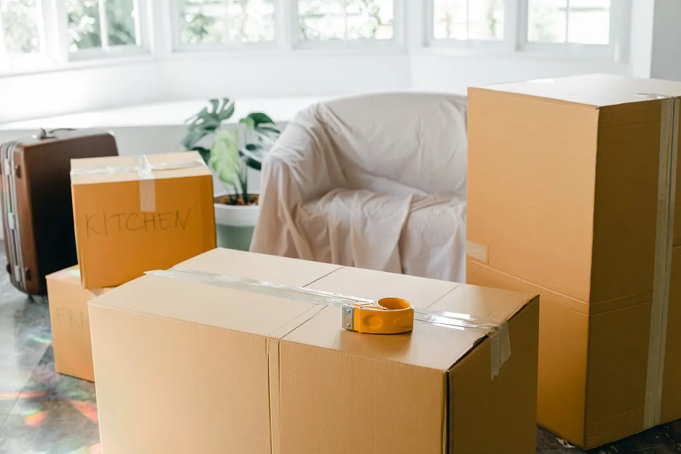 Cardboard cartons and a sofa covered with a white sheet in a room with a large window