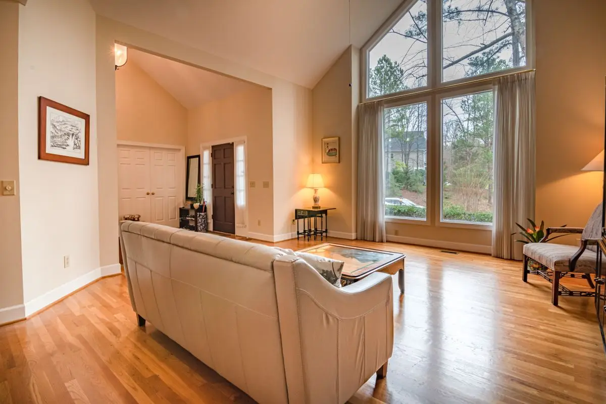 A cream sofa in a bright living room, aimed at a wide doorway with hardwood continuing into the next room