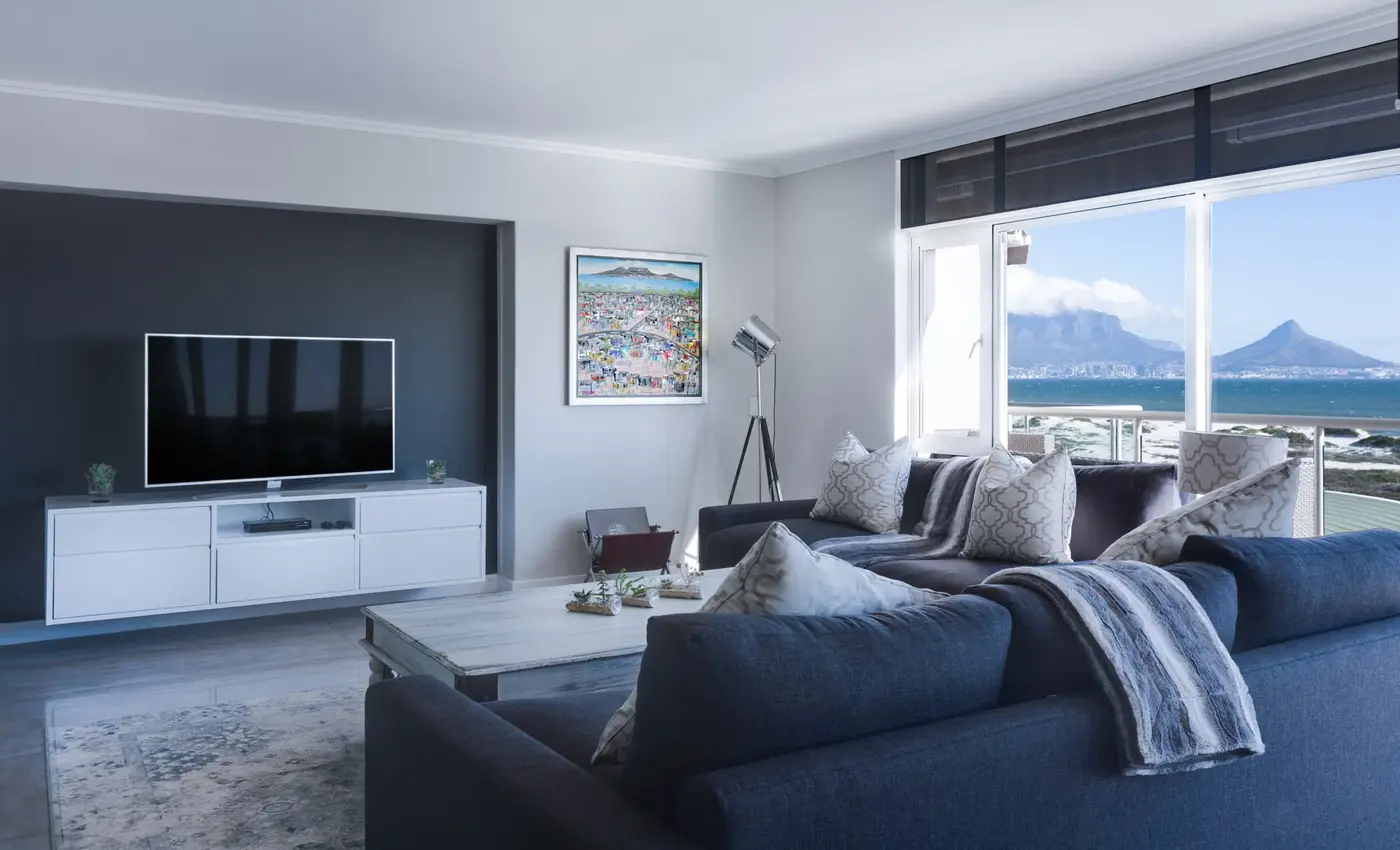 A living room with a navy sofa, a pale wood coffee table, and a white media console under a television