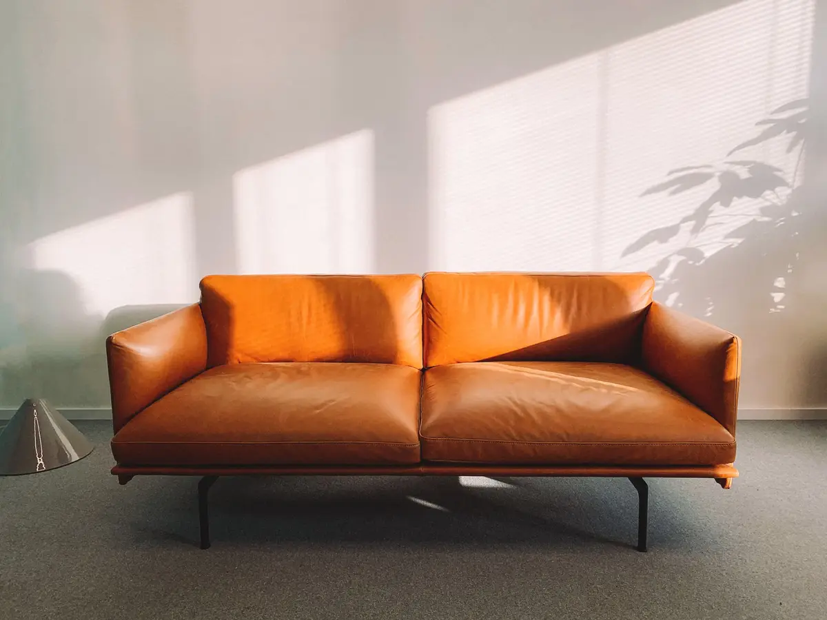 A caramel leather sofa against a white wall in strong afternoon light