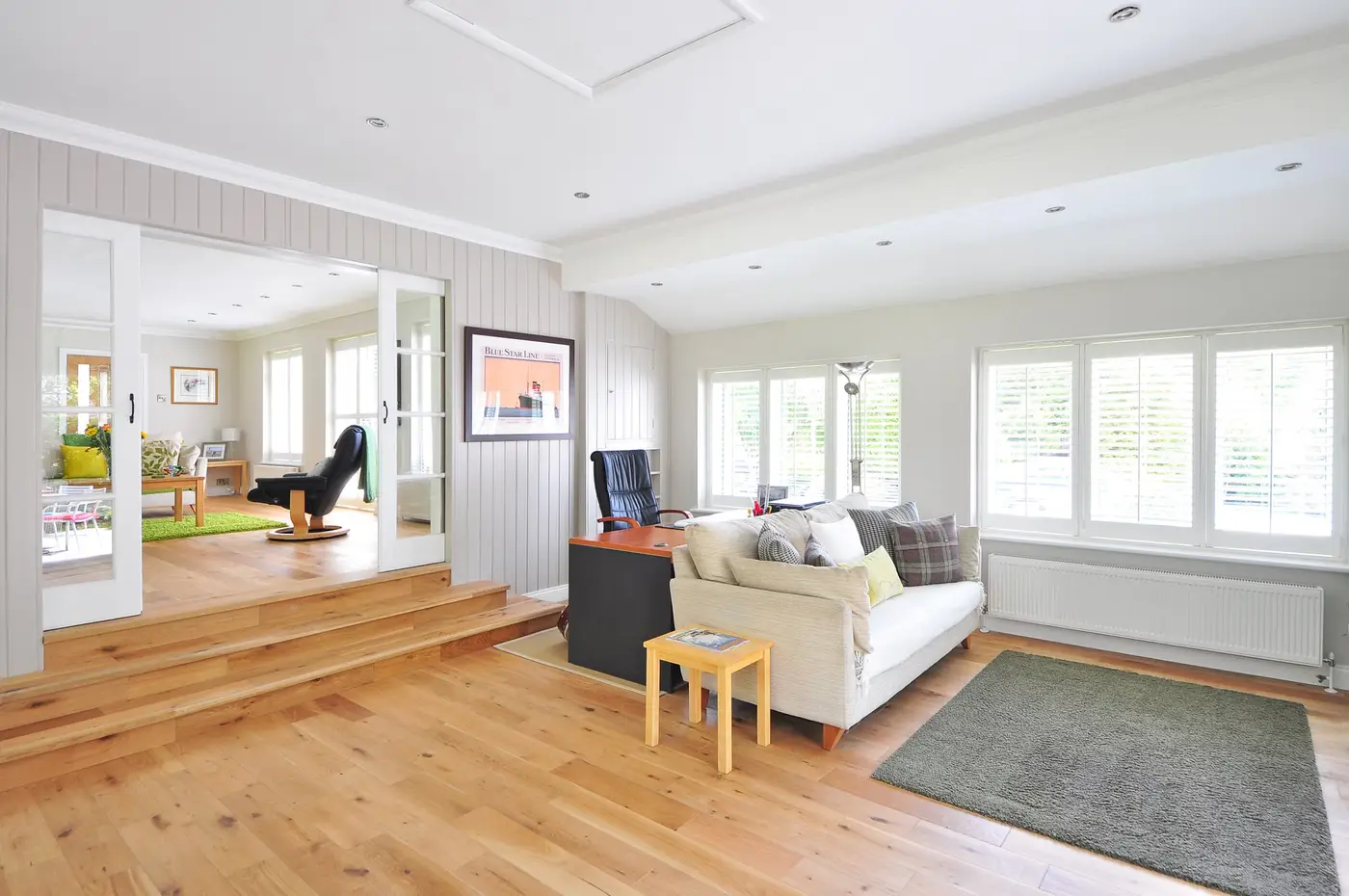 A living room with a step down into an adjacent room and a light sofa on hardwood