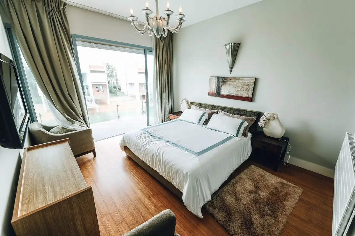 A bedroom with a long wood dresser, a bed, and a window wall