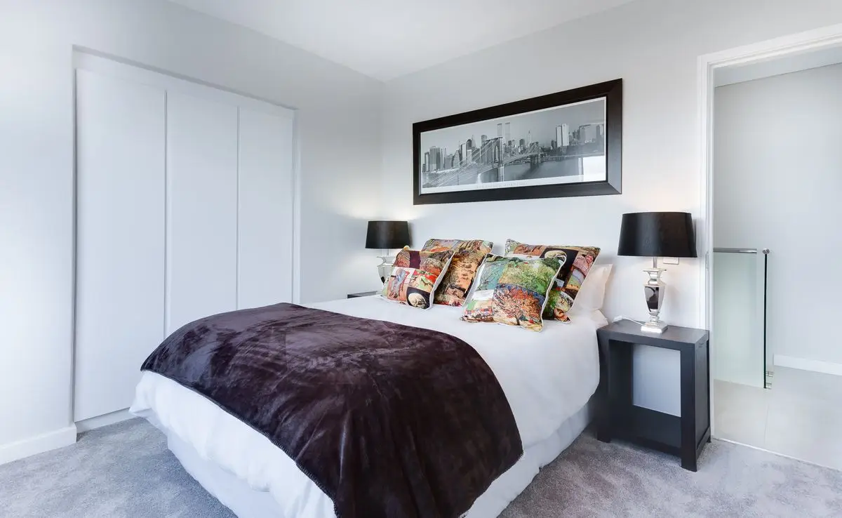 A bedroom with sliding closet doors, a bed, and a dark nightstand
